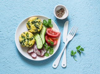 Mini spinach cheddar frittata and vegetables salad on blue background, top view. Breakfast, snack, appetizers plate