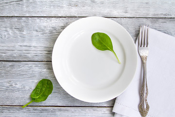 white plate with a fork on a wooden table and two leaves of spinach