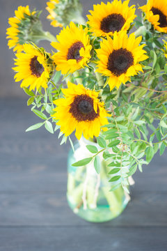 Bouquet of bright sunflowers in a glass jar on a wooden table.