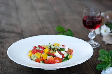 flowers, wine and serving of salad from vegetables on old wooden table