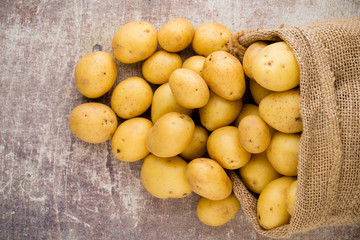 Sack of fresh raw potatoes on wooden background, top view.