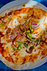 Close up of pizza with bacon and green spicy pepper on a plate on a blue tablecloth. Top view.