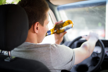 Drunk young driver drinking a bottle of alcohol during driving the car, campaign picture, do not drink alcohol when you drive