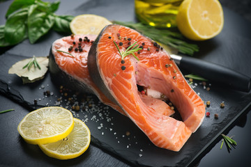 Salmon. Raw trout fish steak with herbs and lemon on black slate background. Cooking, seafood. Healthy eating concept