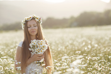 Fototapeta na wymiar Beautiful girl outdoors with a bouquet of flowers in a field of white daisies,enjoying nature. Beautiful Model with long hair in white dress having fun on summer Field with blooming flowers