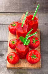 Fresh tomatoes and tomato juice colorful arrangement in drinking glasses with green straws overhead on cutting board in studio