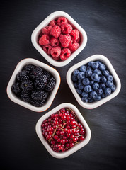 Berries arrangement colorful overhead in four ceramic jars on rustic black table in studio