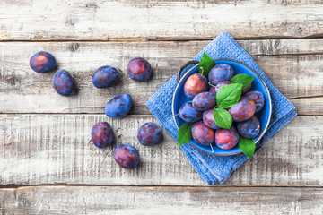 Plums on blue plate and cloth overhead on wooden table