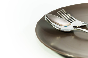 Shiny stainless fork and spoon on brown plate isolated on white background.