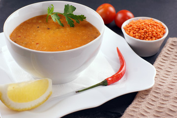 Lentil soup in a plate, next to vegetables and a slice of lemon