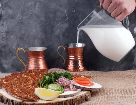 Lunch with Turkish tortilla Lagmajun, a man's hand pours a Turkish national drink ayran in special dishes