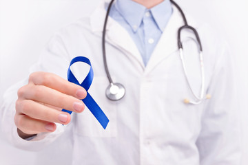 Oncological disease concept. Doctor wearing white coat and stethoscope holding dark blue ribbon as a symbol of bowel cancer.