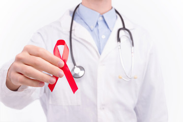 Oncological disease concept. Doctor wearing white coat and stethoscope holding red ribbon as a symbol of aids.