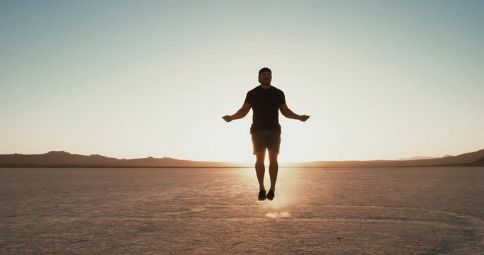 Slow motion: Athletic man working out outside in desert at sunset jumping rope 