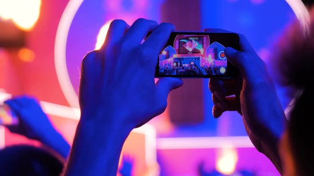 Unrecognizable hands silhouette taking photo or recording video of live music concert with smartphone. Photography, entertainment and technology concept