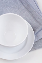 Empty white plate and bowl on a stack of gray napkins on a table.
