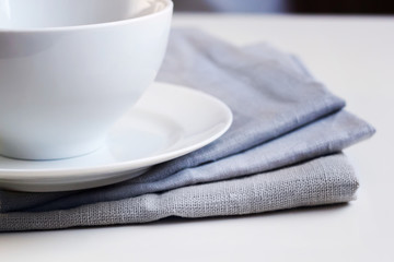 Empty white plate and bowl on a stack of gray napkins on a table.
