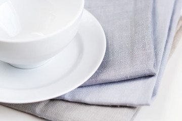 Empty white plate and bowl on a stack of gray napkins on a table.