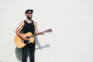 Guitar player singing outside. Hipster guitar player with beard and black clothes