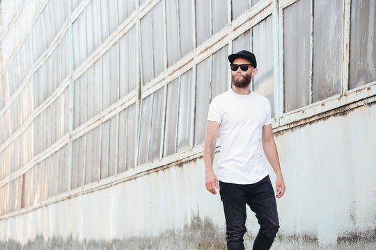 Hipster handsome male model with beard wearing white blank t-shirt with space for your logo or design in casual urban style