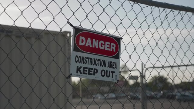 A panning shot of a Danger Construction sign on a chain link fence.