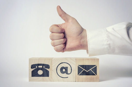 Contact us. Businessman's hand giving thumbs up for communications icons on wooden blocks.