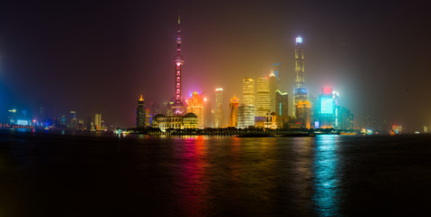 Shanghai skyline glowing in a misty night, reflecting in Huangpu river