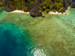 The azure blue sea. Top view of a tropical island with palm trees and blue clear water. Aerial view of a white sand beach and boats over a coral reef. The island of Palawan, Philippines.