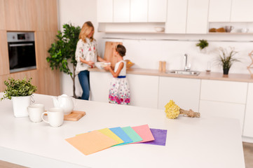 Daughter and mother blur on the back side. On the table in the kitchen lie rags for cleaning of different colors