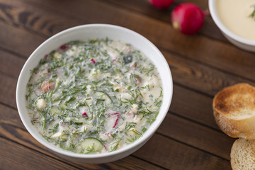 Summer yoghurt cold soup with radish, cucumber, and dill on wooden table. Okroshka.