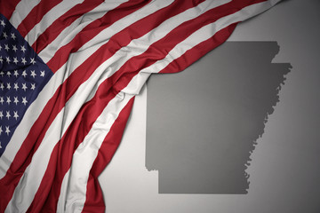 waving national flag of united states of america on a gray arkansas state map background.