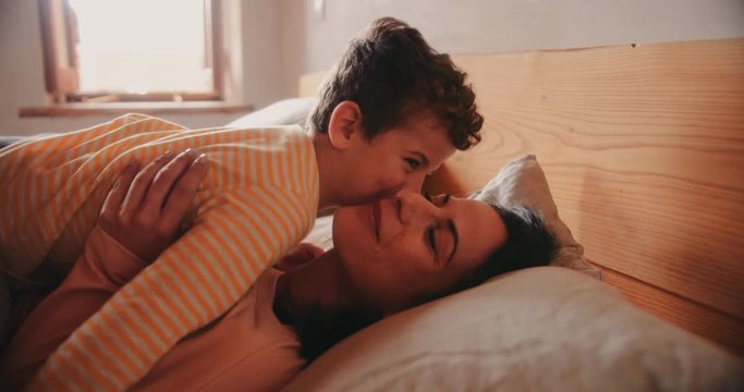 Young son kissing mother in bed in the morning