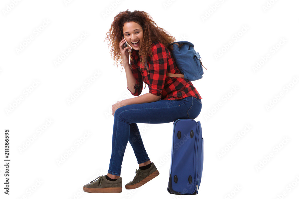 Wall mural Side portrait of happy travel woman sitting on suitcase and talking on cellphone