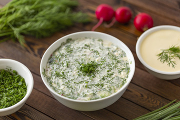 Summer yoghurt cold soup with radish, cucumber, and dill on wooden table. Okroshka.