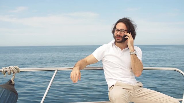 Young bearded businessman talking on smartphone on a luxury yacht, enjoying with a magnificent view of the sea.