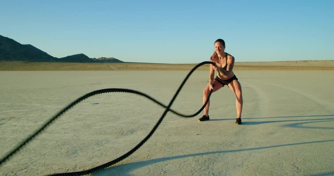Athletic woman doing crossfit battle rope workout outside in desert 