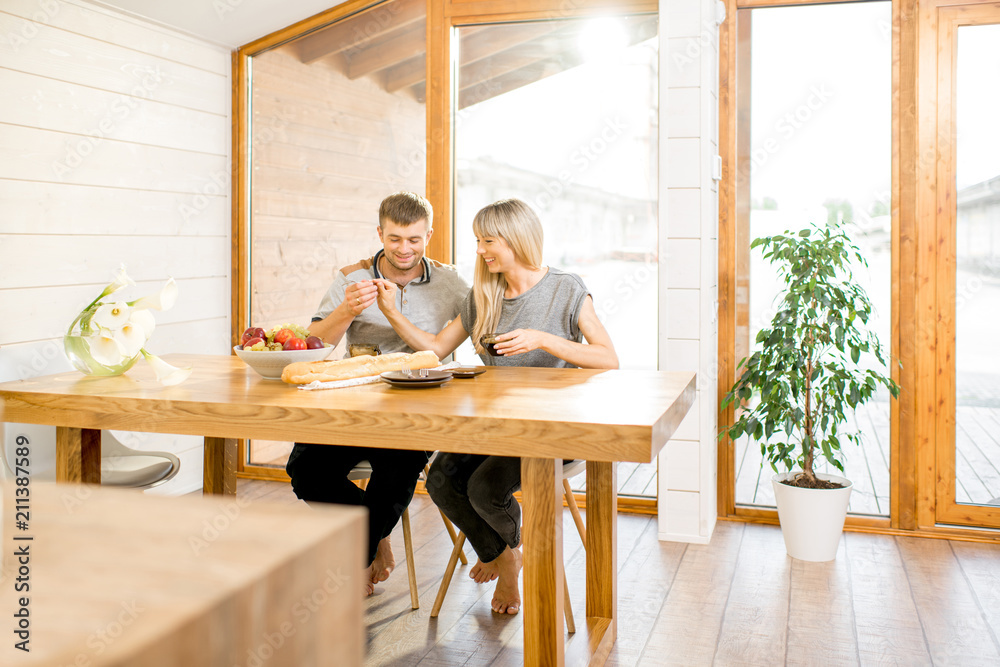 Wall mural young and happy couple having a breakfast sitting at the wooden table in the modern country house wi