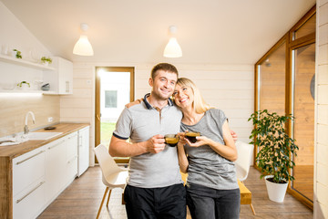 Portrait of a young and happy couple standing together with coffee at the dining room of the modern wooden country house
