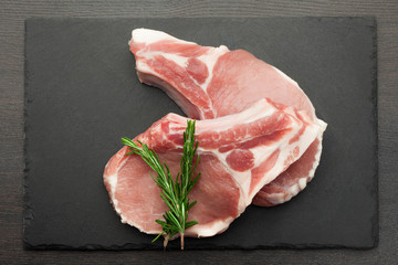 fresh raw meat with rosemary on black slate, on dark background, pork, beef, chop on a bone