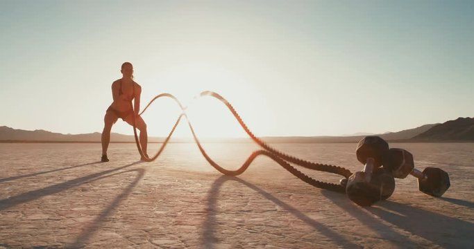 Athletic woman doing crossfit battle rope workout outside at sunset in desert 
