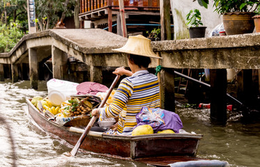 Woman rowing away with canoe full of fruits and vegatables in the Bangkok floating market