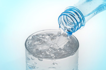 Pouring water from bottle into glass on blue background.