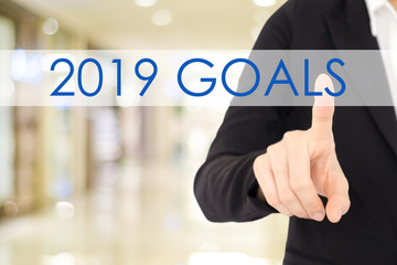 Businesswoman hand touching 2019 goals button over blur office background, banner with copy space, annual plan for success in business concept