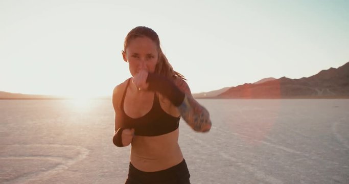 Woman boxing at sunset outside in desert punching at camera 