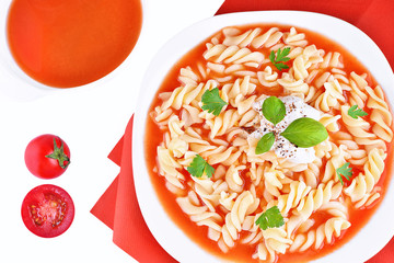 Delicious fresh traditional homemade tomato soup with noodles on white plate and red tablecloth in the background. Decorative colorful photo of a healthy polish dinner