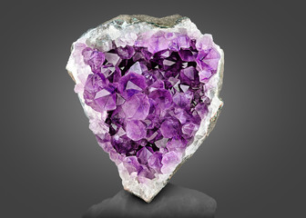 Violet Crystal Stone macro mineral. Purple rough Amethyst quartz crystals geode on gray gradient...