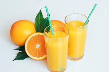 Glasses with orange juice next to orange slices with leaves on a white background.