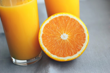 Glass with orange juice next to orange slices on a gray background.