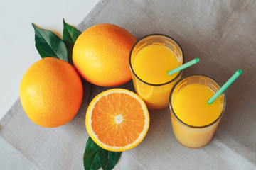 Glasses with orange juice next to orange slices with leaves on a white background with a gray napkin.