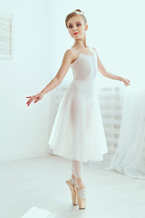 Fototapeta na wymiar Beautiful ballerina is posing and dancing in a white studio full of light. The photo greatly reflects the incomparable beauty of a classical ballet art.